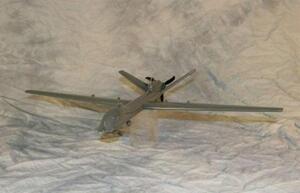 Predator UAV airplane model on a clear acrylic stand, front three-quarter view of long wings, tail and rear propeller