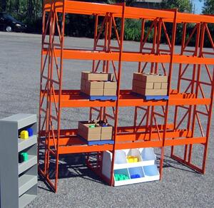 Industrial training model of orange pallet racking with boxed pallets, a gray shelf unit and white parts bins outdoors