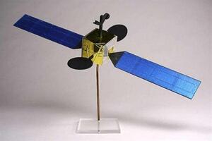 Communications satellite scale model with gold foil body, blue solar arrays and dish reflectors on a clear acrylic stand