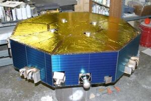 Satellite instrument mockup with gold foil top deck and blue solar cell sides, sensors mounted around the octagonal body