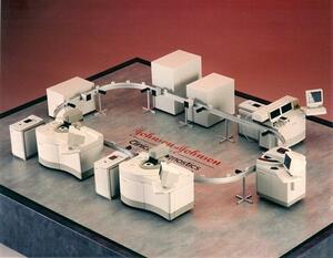 Johnson & Johnson factory model with white analyzer units linked by an elevated loop conveyor track on a gray display base