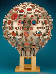 Fusion reactor chamber scale model, a silver sphere covered in ports with red interiors, on a wooden stand