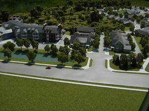 Retirement community model viewed from the main road, with pond, tree-lined entry drive and clustered homes beyond