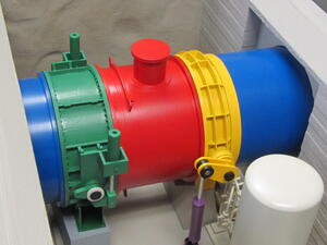 Penstock valve training model with blue pipe, green and yellow valves, red pipe section and white tank in underground room