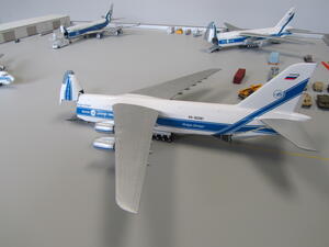 Airport scale model with a large cargo jet, nose visor raised, parked on gray tarmac beside other freighters and vehicles