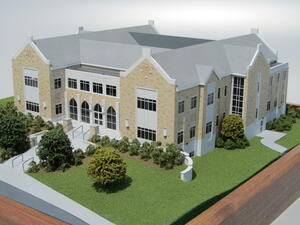 College building scale model seen from the front corner, with brick-textured walls, gray roofs, trees and entry stairs