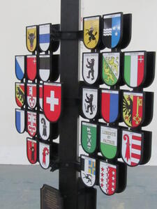 Swiss canton sign close-up at an angle showing cast shields with canton arms on brackets around the black post