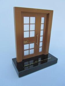 Door model with brown frame, frosted window panes and logo relief, set on a black acrylic base, viewed from the left