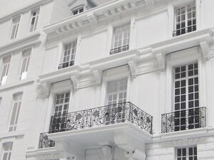 Building facade model close-up showing black brass-etched balcony railings, carved corbels and multi-pane windows