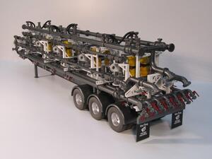 Manifold trailer model from the rear corner, showing triple-axle wheels, stacked piping and red-handled valve outlets
