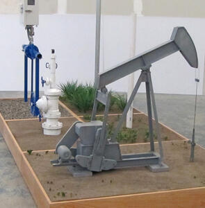 Motorized pumpjack model in an oil field diorama, front three-quarter view of the gearbox, crank and walking beam