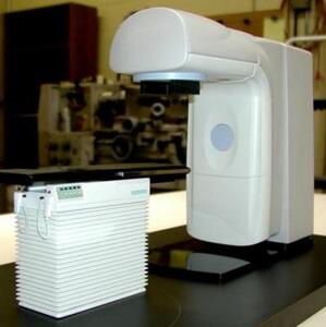 CT scanner model's white overhead gantry arm beside a patient table with pleated bellows base, on a black display base