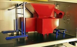 Red shredder with hopper and blue lift frame inside the trailer cutaway model, seen through the open side wall