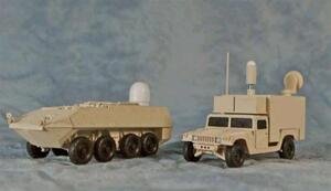 Lockheed military vehicle models: tan 8x8 armored vehicle with radome next to a utility truck with sensor shelter