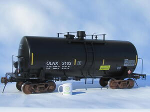 Railroad tank car scale model in side view on a white backdrop, with a KiwiMill mug beside the trucks for scale
