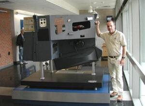 Full-scale MODIS instrument mockup on a raised black display base in a building lobby, a man standing beside it for scale