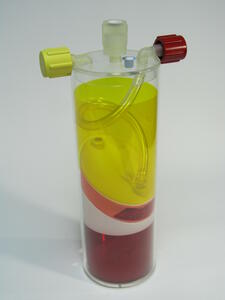 Blood separator scale model at three-quarter angle, yellow plasma and red cell layers inside a clear acrylic tube