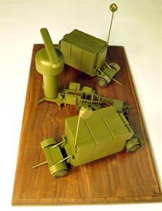 Desktop radar model seen from above, with radar antenna tower, small trailer and two equipment trailers on a walnut base