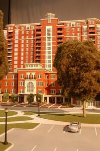 High-rise apartment building architectural model seen from the parking lot, with lawn, lamp posts and a silver car