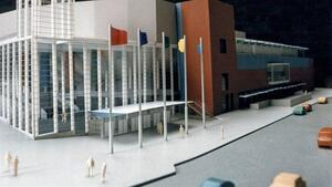 Arena architectural model showing glass colonnade entrance, canopy, flagpoles, scale figures and cars on the street