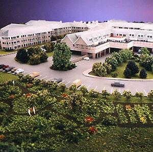 Retirement community architectural model from above, showing building wings, parking lot, trees and garden plots
