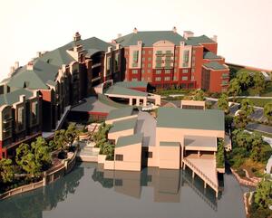 Retirement community site model with brick residential wings, green roofs and a low-rise building reflected in a glossy lake