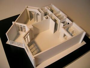 All-white apartment floor plan model with roof removed, showing walls, doorways, window frames and a railed balcony