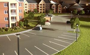 Housing development model at eye level, showing a curved parking lot, lamp posts, trees and brick apartment buildings