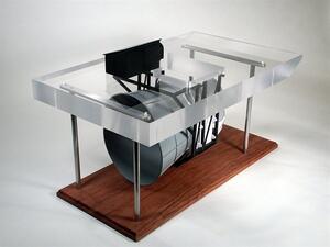 Barge turbine scale model with shrouded turbine hung beneath a clear acrylic barge on a wood base, seen from above