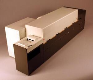 Digital press scale model seen at an angle from the feed end, showing the white top cover and paper input tray