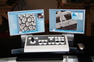 Orion ion beam microscope model workstation with two monitors showing sample images and a joystick control panel