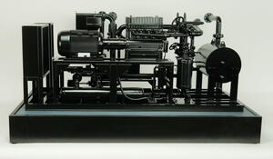 Industrial heat pump scale model, front view of black skid with motor, compressor and piping on a display base