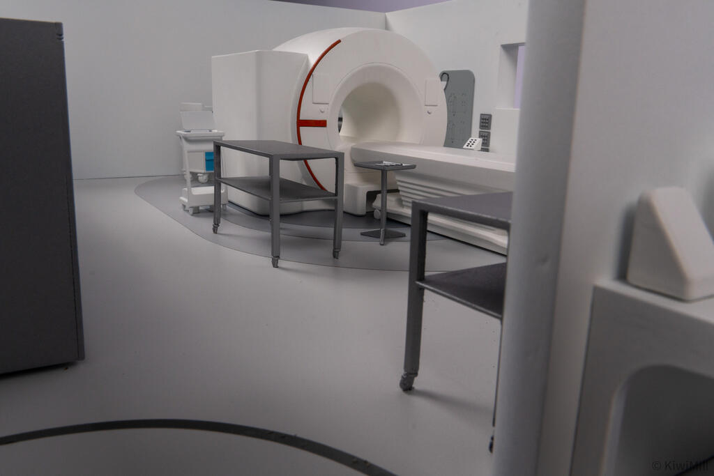 Low eye-level view across the procedure room floor toward the MRI scanner, steel instrument tables and side cart
