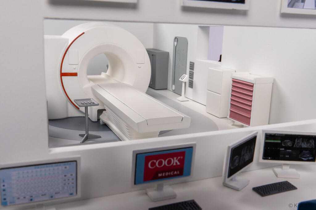 Angled view through the observation window of the MRI scanner, patient table and pink drawer cart in the procedure room