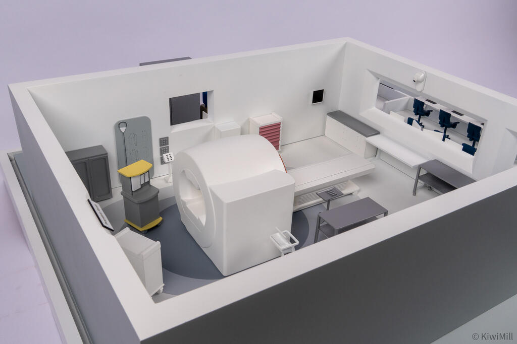 Open-top procedure room from above at an angle, showing the scanner rear, yellow-topped cart and wall equipment