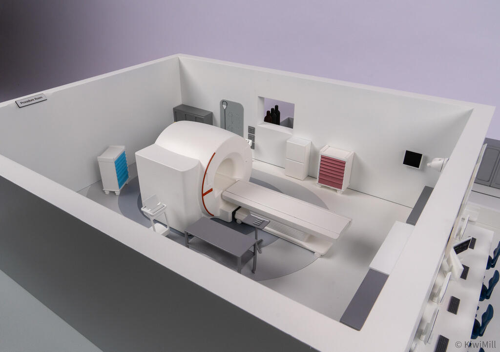 Procedure room corner view with MRI scanner, extended patient table, blue and pink drawer carts and room sign