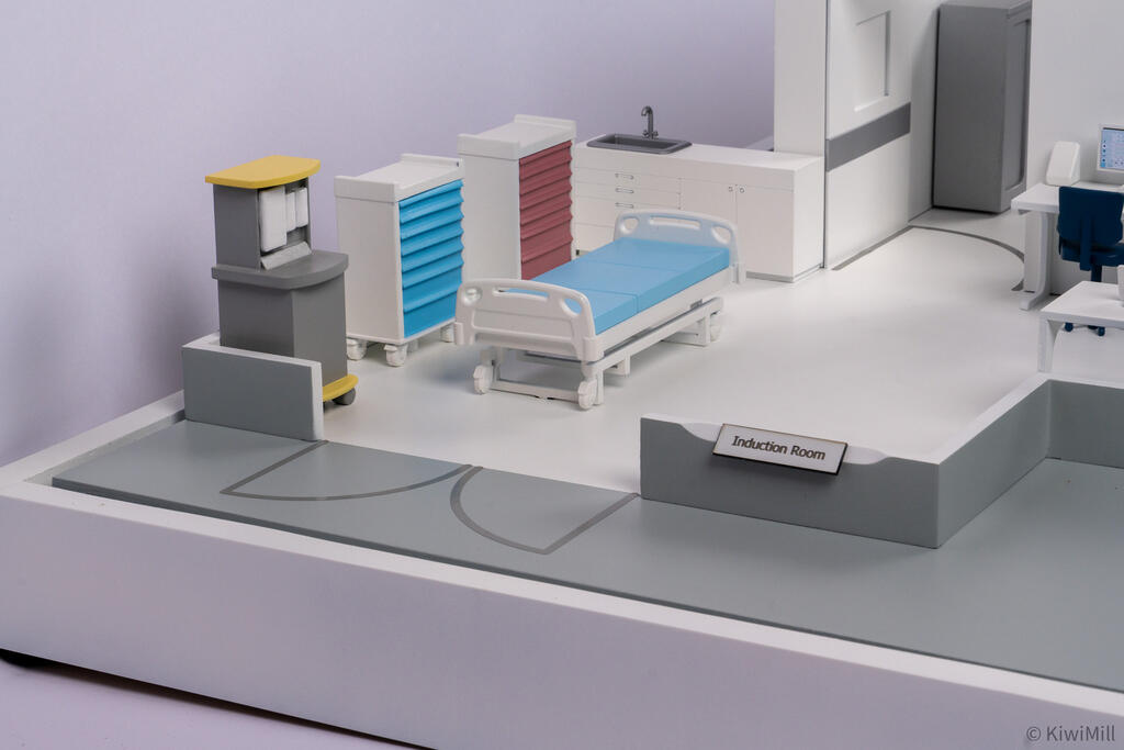 Close-up of the induction room with blue-covered hospital bed, color drawer carts, sink counter and room label