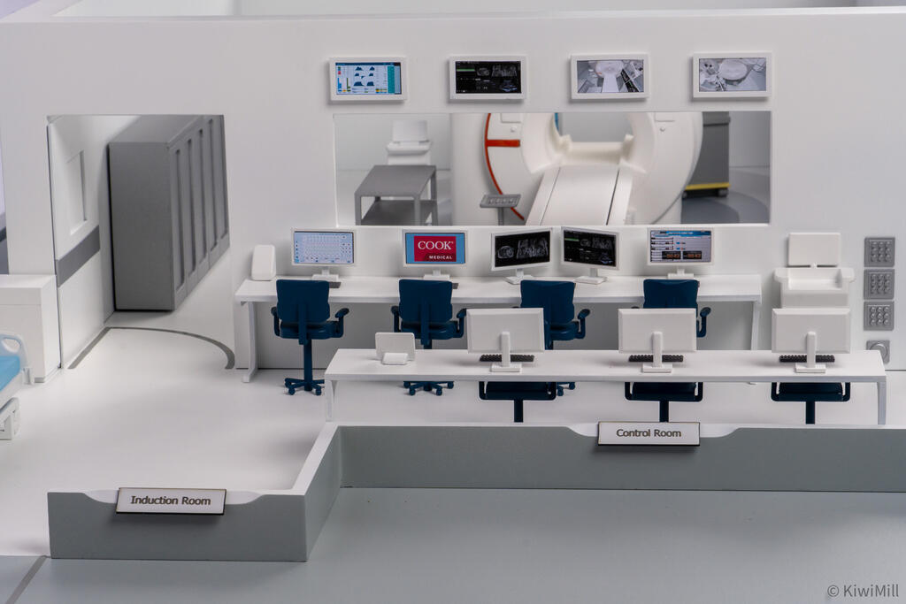 Front view of the control room's two rows of workstations below wall monitors, with labeled room edges