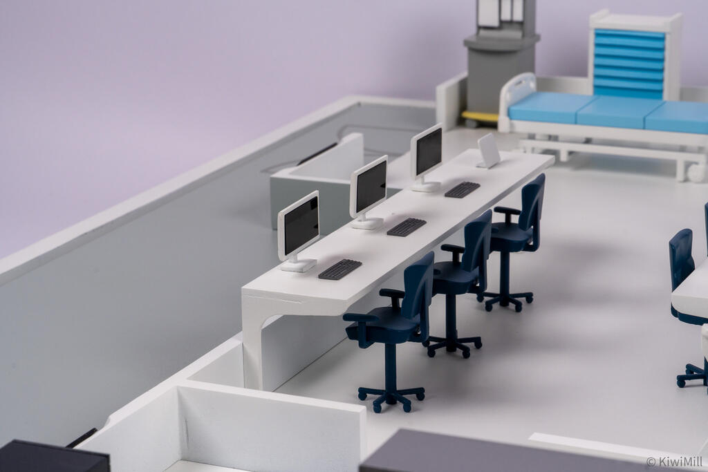 Close-up of a workstation desk with three monitors, keyboards and blue office chairs near the induction room